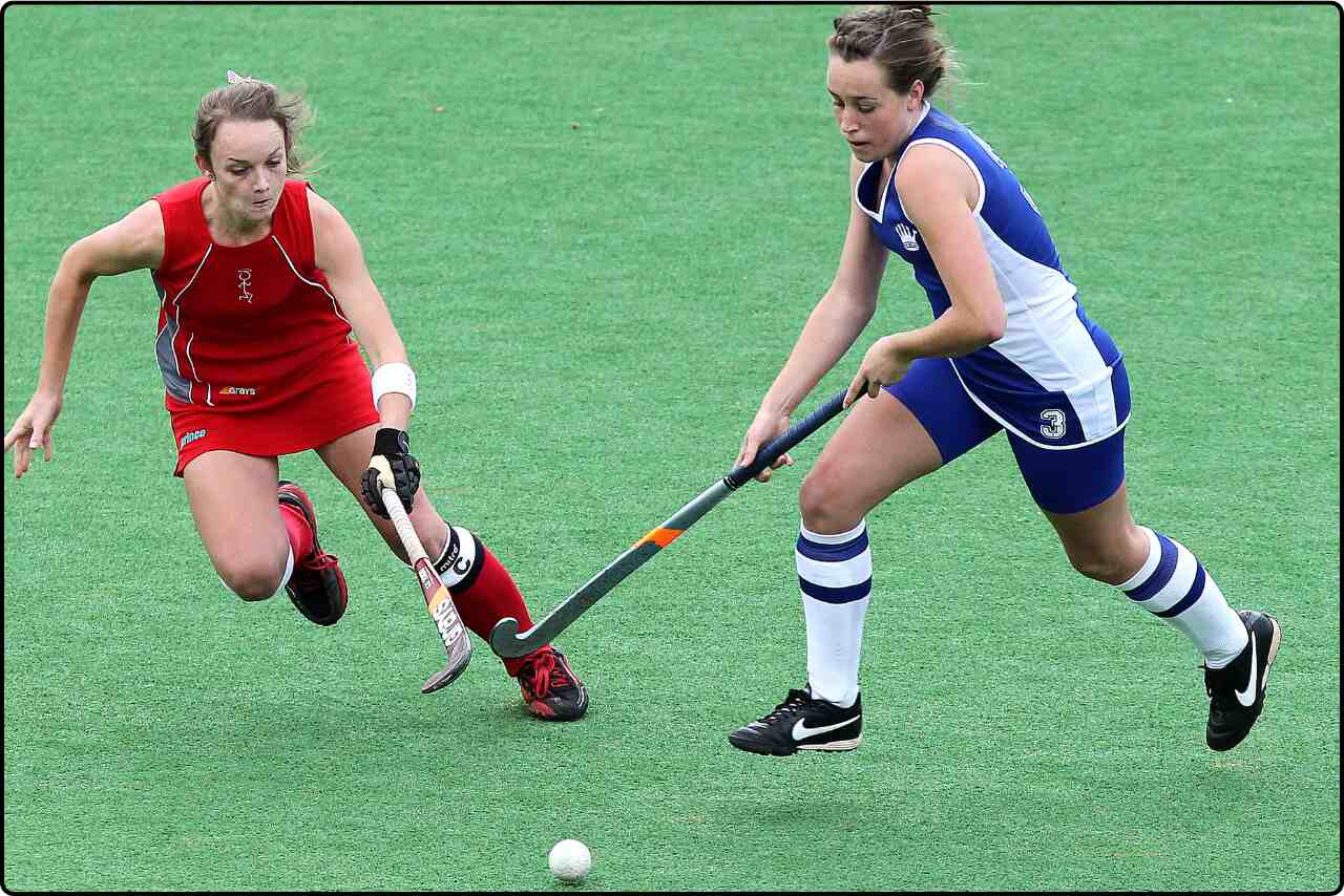 Action shot of two women battling for a goal, one attempting to score while the other defends in hocky game.